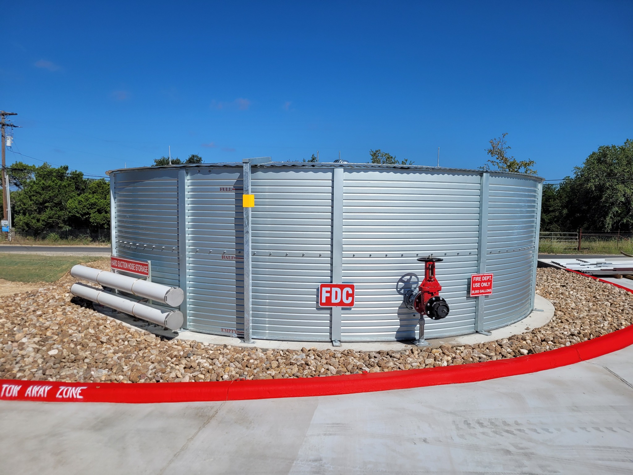 Completed corrugated steel fire-water tank with fire department connection, OS&Y valve, signage, and hard suction hose storage